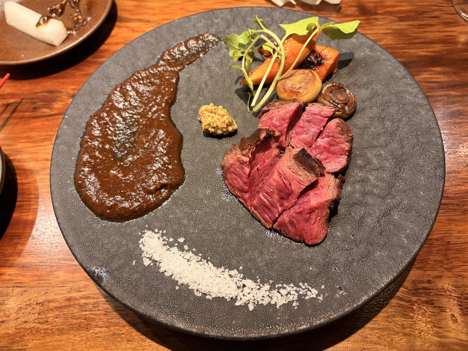 満月堂のサガリ。レアに焼いてスライスされた牛肉に、粒マスタード、塩、焼き野菜が添えられている