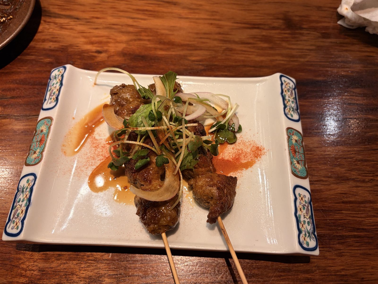 満月堂のラム串。染付の角皿に2本、白髪ねぎと赤玉ねぎ、唐辛子粉が添えられている