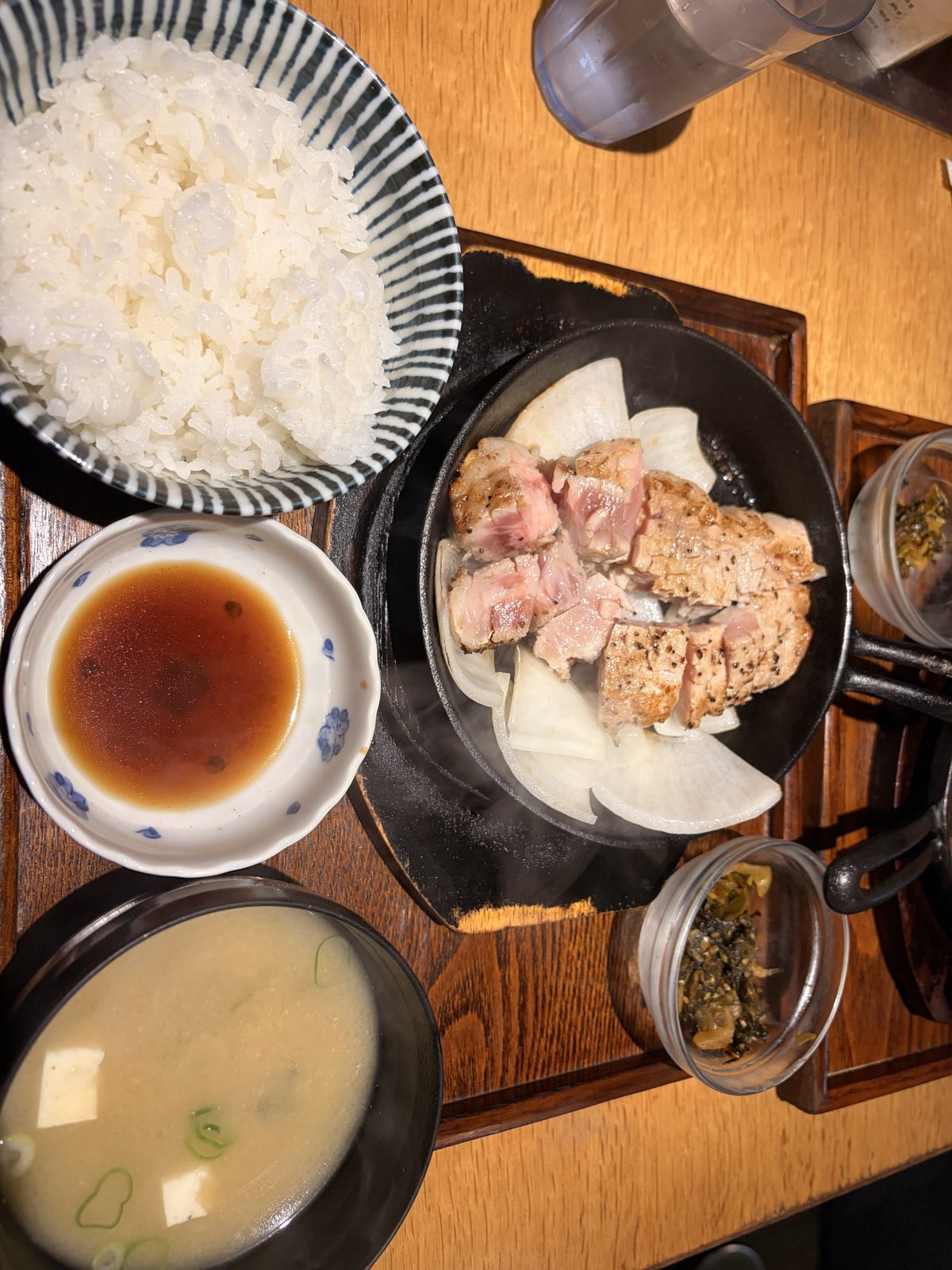 豚ステーキ十一（といち）住吉店の豚ステーキ。鉄板の上に玉ねぎと大根、その上に表面を焼いた豚肉。ごはん、味噌汁、たれ、高菜